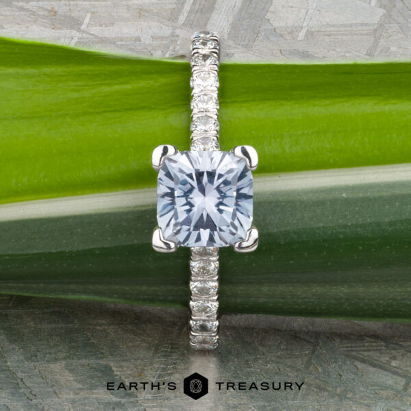 The "Meissa" ring in 14K white gold with 1.47-carat Montana sapphire The "Meissa" ring in 14K white gold with a 1.47-carat Montana sapphire and diamond band rests on a green leaf, with the Earth's Treasury logo visible at the bottom of the image.