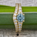 The "Arethusa" ring in 18K yellow gold features a 1.33-carat Montana sapphire, paired with the matching "Arethusa" band in 18K gold, elegantly displayed on a green plant stem above the Earth's Treasury logo.