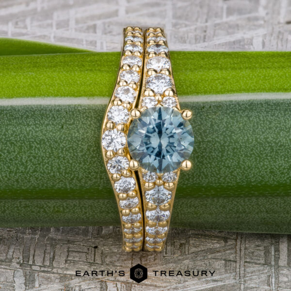 The "Arethusa" ring in 18K yellow gold with 1.33-carat Montana sapphire, alongside the "Arethusa" band in 18K yellow gold The "Arethusa" ring in 18K yellow gold features a 1.33-carat Montana sapphire, paired with the matching "Arethusa" band in 18K gold, elegantly displayed on a green plant stem above the Earth's Treasury logo.