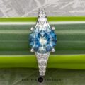 The "Arethusa" ring in platinum features a 2.65-carat round Montana sapphire and smaller clear stones along the band, shown on a green leaf with "Earth's Treasury" below—an exquisite, nature-inspired jewelry design.