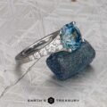 The "Arethusa" ring in platinum, featuring a 2.65-carat Montana sapphire, is placed on a rough blue stone atop a textured gray surface with the "Earth's Treasury" logo at the bottom.