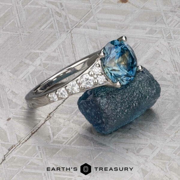 The "Arethusa" ring in platinum with 2.65-carat Montana sapphire The "Arethusa" ring in platinum, featuring a 2.65-carat Montana sapphire, is placed on a rough blue stone atop a textured gray surface with the "Earth's Treasury" logo at the bottom.
