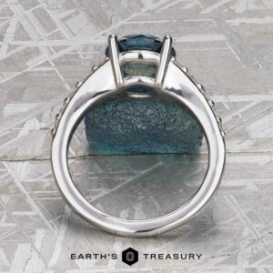 The "Arethusa" ring in platinum, featuring a 2.65-carat Montana sapphire, is displayed upright on a textured surface with the Earth's Treasury logo at the bottom.