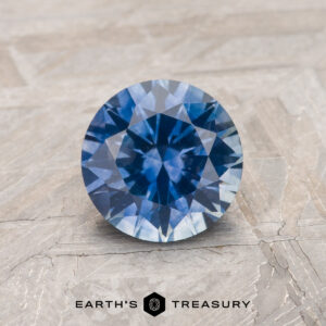 A 1.20-carat violet-blue Montana sapphire (heated) is shown on a textured surface, with "EARTH'S TREASURY" displayed at the bottom.
