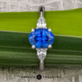 A platinum "Merope" ring featuring a 1.42-carat Ceylon sapphire and two pear-shaped clear stones, displayed on a green leaf background with "Earth's Treasury" branding below.