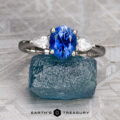 The "Merope" ring in platinum showcases a 1.42-carat Ceylon sapphire between two white stones, displayed on rough blue stone. Text reads “Earth’s Treasury.”.