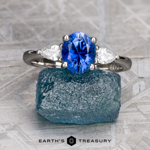 The "Merope" ring in platinum with 1.42-carat Ceylon sapphire The "Merope" ring in platinum showcases a 1.42-carat Ceylon sapphire between two white stones, displayed on rough blue stone. Text reads “Earth’s Treasury.”.