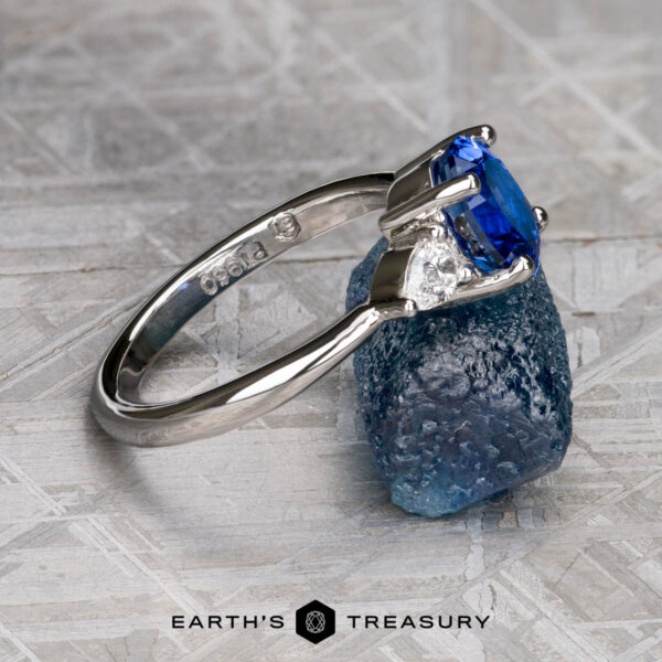 The "Merope" ring in platinum with 1.42-carat Ceylon sapphire The "Merope" ring in platinum, featuring a 1.42-carat Ceylon sapphire center, is showcased on a rough blue gem against a geometric patterned backdrop.