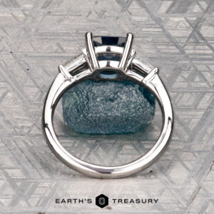 The Le Renard, Yann ring, featuring a rectangular blue gemstone set in silver, stands upright on textured blue stone with the Earth's Treasury logo beneath.