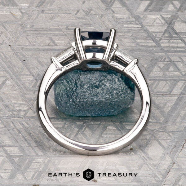 Le Renard, Yann The Le Renard, Yann ring, featuring a rectangular blue gemstone set in silver, stands upright on textured blue stone with the Earth's Treasury logo beneath.