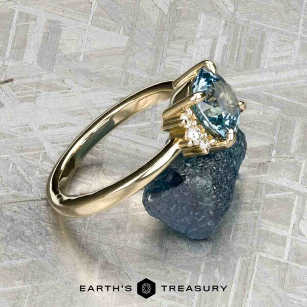 The "Hesperia" ring in 14K yellow gold with 2.21-carat Montana sapphire A 14K yellow gold "Hesperia" ring with a 2.21-carat Montana sapphire is displayed on raw blue crystal, with the Earth's Treasury logo visible below.