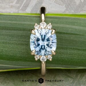 The "Hesperia" ring in 14K yellow gold features a 2.21-carat Montana sapphire and small round diamonds, shown on a green leaf with the Earth's Treasury logo below.