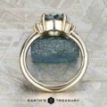 The "Hesperia" ring in 14K yellow gold showcases a 2.21-carat Montana sapphire and side baguette stones, shown upright with a rough blue mineral and the Earth’s Treasury logo in the background.