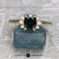The "Hesperia" ring in 14K yellow gold showcases a 1.55-carat Australian sapphire with accent diamonds, displayed on a rough bluish stone above the "EARTH'S TREASURY" logo.