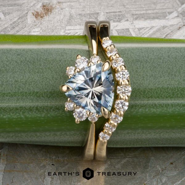 The "Hesperia" ring in 18K yellow gold with 1.44-carat Montana sapphire, alongside the "Hesperia" band in 18K yellow gold The "Hesperia" ring in 18K yellow gold with a 1.44-carat Montana sapphire is paired with the matching "Hesperia" band, both shown on a green surface.