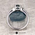 The "Mavis" ring in 14K white gold with a 1.02-carat Montana sapphire is shown upright on a blue stone, with the "Earth's Treasury" logo beneath on a textured background.