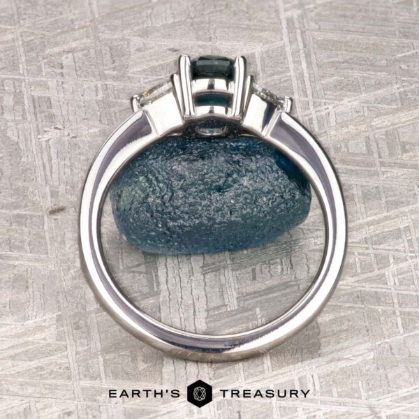 The "Mavis" ring in 14K white gold with 1.02-carat Montana sapphire The "Mavis" ring in 14K white gold with a 1.02-carat Montana sapphire is shown upright on a blue stone, with the "Earth's Treasury" logo beneath on a textured background.