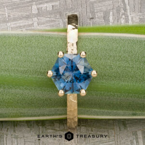 The "Snowflake" ring in 18K yellow gold, hammered and polished, featuring a 1.80-carat Montana sapphire, stands upright on a green leaf with the Earth's Treasury logo below—evoking the style of Snowflake Solitaire.