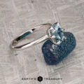 The "Nelisa" ring in 14K white gold with a 1.51-carat Montana sapphire rests on a rough blue stone atop a textured gray surface, with Earth's Treasury logo at the bottom.