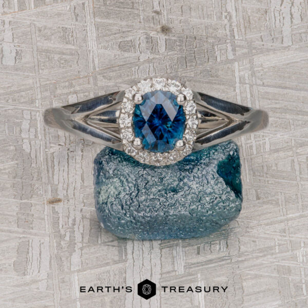 The "Diana" ring in platinum with 0.87-carat Montana sapphire The "Diana" ring in platinum features a 0.87-carat Montana sapphire framed by a halo of diamonds, beautifully displayed on a rough blue stone atop a textured light gray surface.