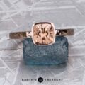 The Stackable "Emma" ring in 14K rose gold, hammered, with a 1.39-carat Mahenge garnet is shown upright on a rough blue stone against a silvery textured background.
