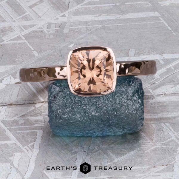 The Stackable "Emma" ring in 14K rose gold, hammered, with 1.39-carat Mahenge garnet The Stackable "Emma" ring in 14K rose gold, hammered, with a 1.39-carat Mahenge garnet is shown upright on a rough blue stone against a silvery textured background.