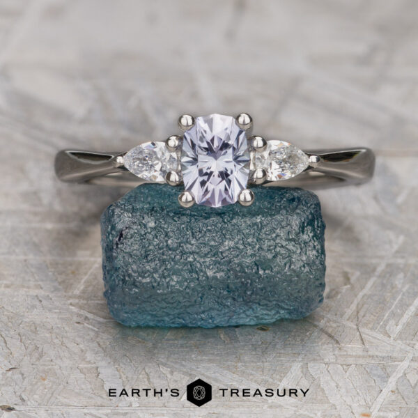 The "Clematis" in platinum with 0.74-carat Montana sapphire The "Clematis" ring in platinum, featuring a 0.74-carat rectangular Montana sapphire and two pear-shaped side stones, is displayed upright on rough blue crystal with the Earth's Treasury logo below, elegantly highlighting each gem.