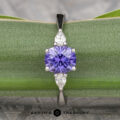 The "Clematis" Ring in platinum features a 1.62-carat round Madagascar sapphire at the center, accented by two pear-shaped clear stones, shown displayed on a green leaf.
