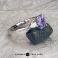 The "Clematis" Ring in platinum with a 1.62-carat Madagascar sapphire rests on a rough blue-green mineral, set against a patterned gray background.