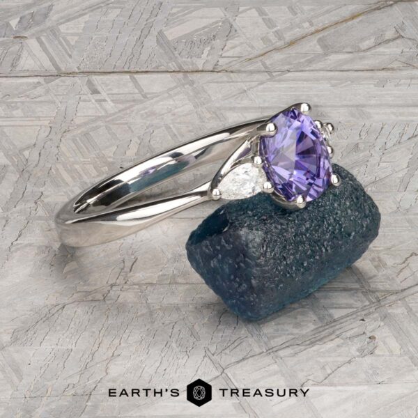 The "Clematis" Ring in platinum with 1.62-carat Madagascar sapphire The "Clematis" Ring in platinum with a 1.62-carat Madagascar sapphire rests on a rough blue-green mineral, set against a patterned gray background.