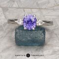 The "Clematis" Ring in platinum, featuring a 1.62-carat Madagascar sapphire and two pear-shaped clear stones, is displayed on a rough blue-green mineral.