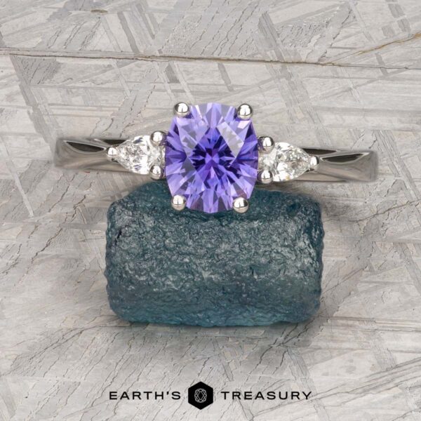 The "Clematis" Ring in platinum with 1.62-carat Madagascar sapphire The "Clematis" Ring in platinum, featuring a 1.62-carat Madagascar sapphire and two pear-shaped clear stones, is displayed on a rough blue-green mineral.