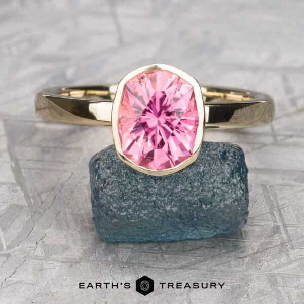 The Stackable "Emma" ring in 14K yellow gold with 2.02-carat California Tourmaline A 14K yellow gold Stackable "Emma" ring with a 2.02-carat California Tourmaline is displayed standing on a rough blue-green stone, with the Earth's Treasury logo visible below.