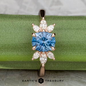 Showcasing the "Liriope" ring in 14k rose gold, this piece features a 1.40-carat Montana sapphire at its center with marquise and pear-shaped clear stones, elegantly displayed on a green background.