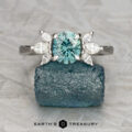 The "Liriope" ring in 14k white gold with a 1.23-carat Montana sapphire and four marquise-cut clear stones rests on rough blue mineral. "EARTH'S TREASURY" logo appears below, showcasing unique rings inspired by nature's beauty.