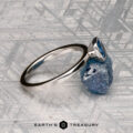 A McMinn, Richard and Gomez, Eric solitaire ring with an oval blue gemstone sits on a rough blue stone atop a geometric surface with the "Earth's Treasury" logo—ideal as a stackable or elegant solitaire ring.