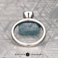 A solitaire ring with a rough blue gemstone is shown on a gray patterned surface, labeled "McMinn, Richard and Gomez, Eric" below.