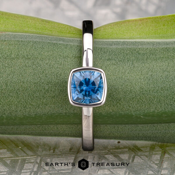 McMinn, Richard and Gomez, Eric A stackable silver ring with a square bezel-set blue gemstone is displayed on a green leaf, with "McMinn, Richard and Gomez, Eric" written below.