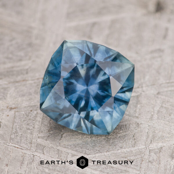 1.82-Carat Blue-Green Montana Sapphire (Heated) A 1.82-carat blue-green Montana sapphire (heated) is displayed on a textured surface with the "EARTH'S TREASURY" logo and text beneath it.