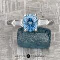 The "Mandevilla" ring in platinum features a 1.61-carat Montana sapphire cushion-cut center stone and two baguette diamonds, displayed on a blue mineral with the Earth's Treasury logo below.