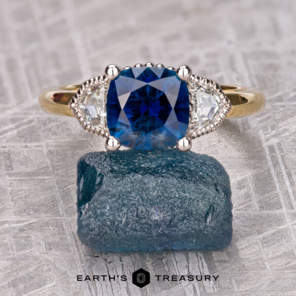 The "Celaeno" ring in 18K yellow gold and platinum with 3.87-carat Montana sapphire The "Celaeno" ring in 18K yellow gold and platinum, featuring a 3.87-carat Montana sapphire, rests elegantly on a rough blue gemstone.
