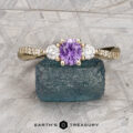 The "Lonicera" ring in 14K yellow gold features a 0.66-carat round Umba sapphire center, two clear side stones, and small diamonds along the band, presented on a blue rough gemstone.