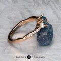 The "Lonicera" ring in 14k rose gold with a 0.93-carat Montana sapphire is displayed beside a rough blue stone on textured gray, with the EARTH'S TREASURY logo below, highlighting nature-inspired jewelry.