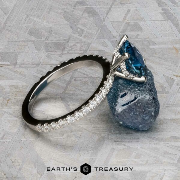 The "Amphitrite" ring in platinum with 1.81-carat Montana sapphire The "Amphitrite" ring in platinum, featuring a 1.81-carat Montana sapphire and diamond accents, is set against a rough blue stone on a textured gray surface. The text "Earth's Treasury" appears below.