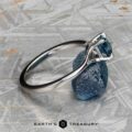 The "Cybele" ring in 18K white gold featuring a 0.96-carat Montana sapphire is displayed atop a raw blue stone on a textured gray surface. The Earth's Treasury logo appears below, capturing Cybele's elegance.