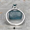 The "Cybele" ring in 18K white gold, featuring a 0.96-carat Montana sapphire, is displayed upright on a patterned gray surface. "Earth's Treasury" appears at the bottom.