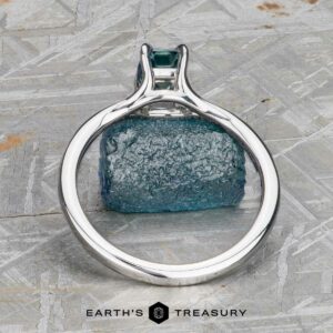 The "Cybele" ring in 18K white gold, featuring a 0.96-carat Montana sapphire, is displayed upright on a patterned gray surface. "Earth's Treasury" appears at the bottom.
