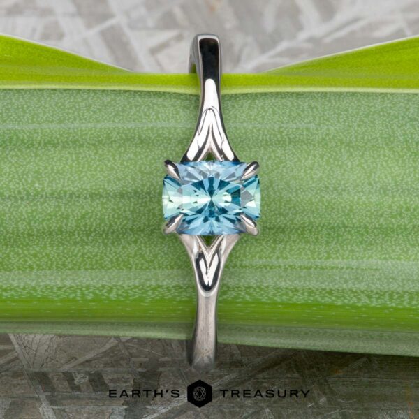 The "Cybele" ring in 18K white gold with 0.96-carat Montana sapphire An 18K white gold "Cybele" solitaire engagement ring with a 0.96-carat Montana sapphire displayed on a green leaf, with the Earth's Treasury logo at the bottom.