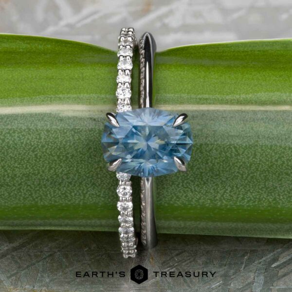 The "Tiara" ring in 18k white gold with 2.85-carat Montana sapphire, alongside the "Kivu" Band in 18k white gold The "Tiara" ring in 18k white gold with a 2.85-carat Montana sapphire and the "Kivu" Band in 18k white gold are displayed side by side on a green surface with the Earth's Treasury logo below.