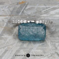 The "Kivu" band in 18k white gold, designed in a Hidden Halo Solitaire style, rests on a rough blue gemstone against a textured gray background, with the Earth's Treasury logo below.